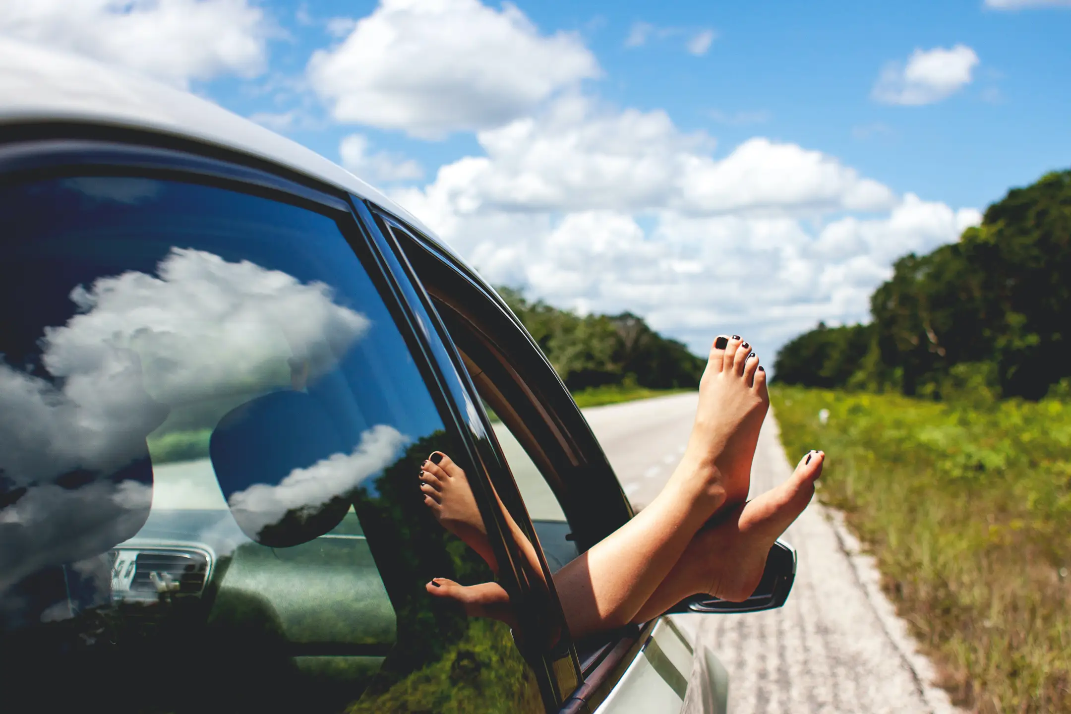 a pair of feet hanging out the window of a car as it travels down a road