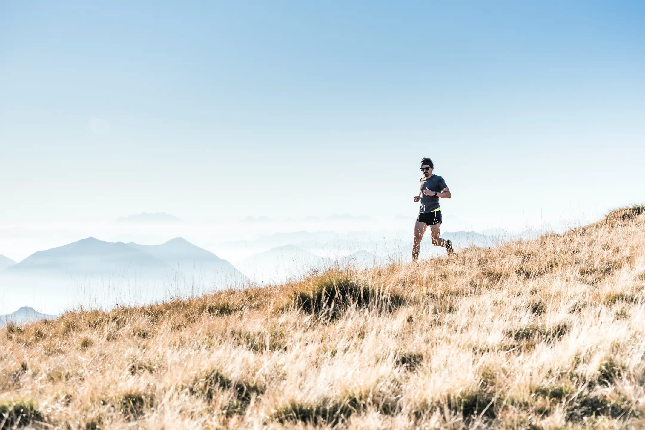 athlete running through field of dry grass mountains in background